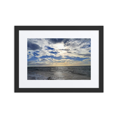 Framed artwork of a seascape with a blue sky and clouds.