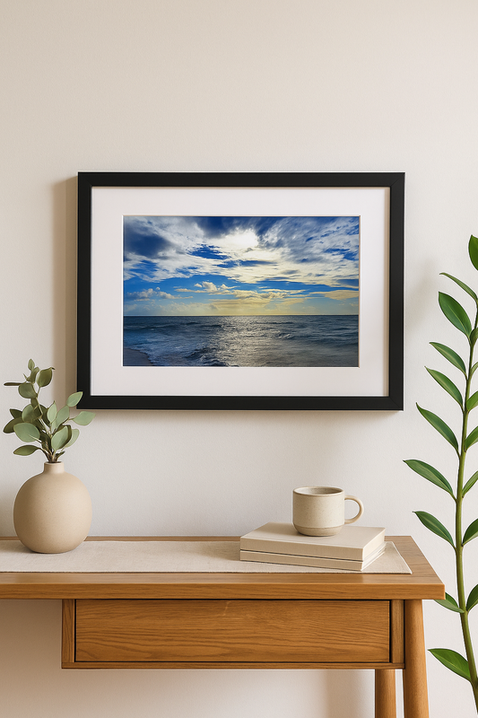 Framed artwork of a blue sky and ocean on a wall above a wooden desk with decor items.