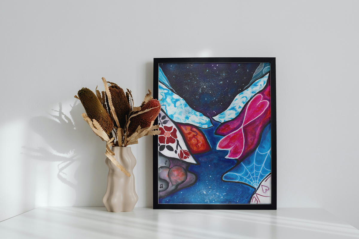 Framed abstract artwork on a white wall with a vase of dried flowers.